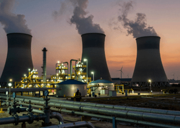 Natural gas power plant at dusk with steam cooling towers, industrial pipelines, and a utility worker on the horizon